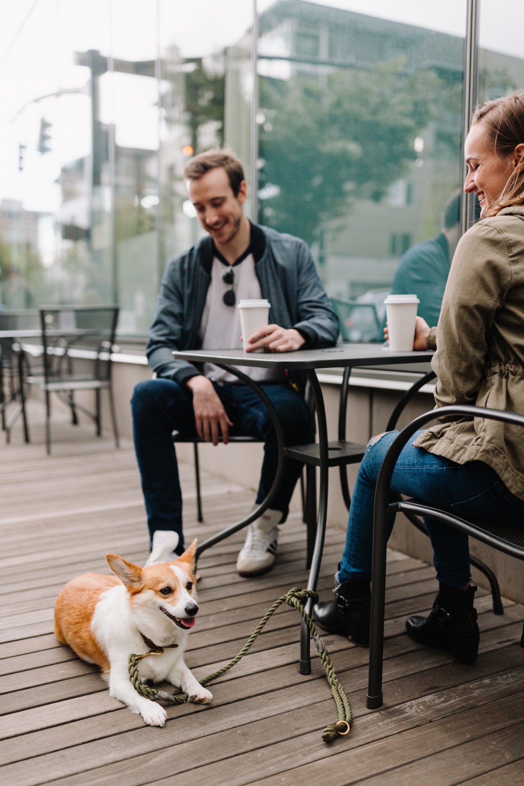 Two men sitting at an outdoor table at a restaurant. A Corgi dog is resting on the ground next to them
