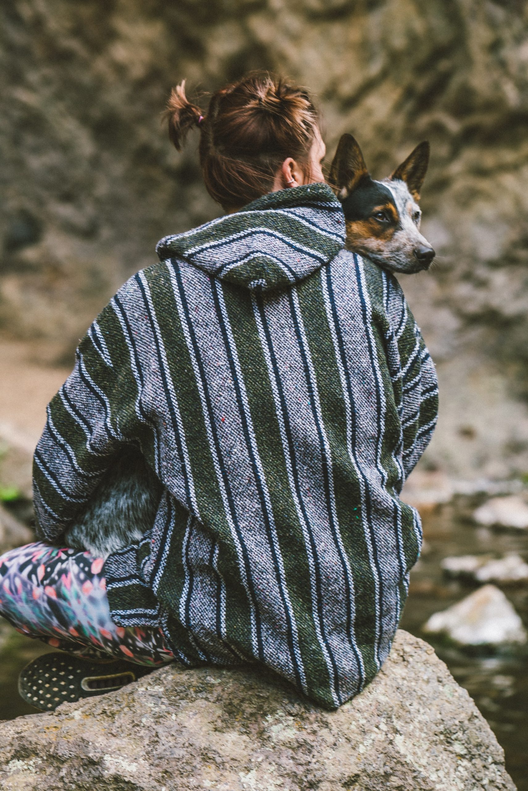Man wearing a mexican-styled sweater with a dog resting its head on his shoulder