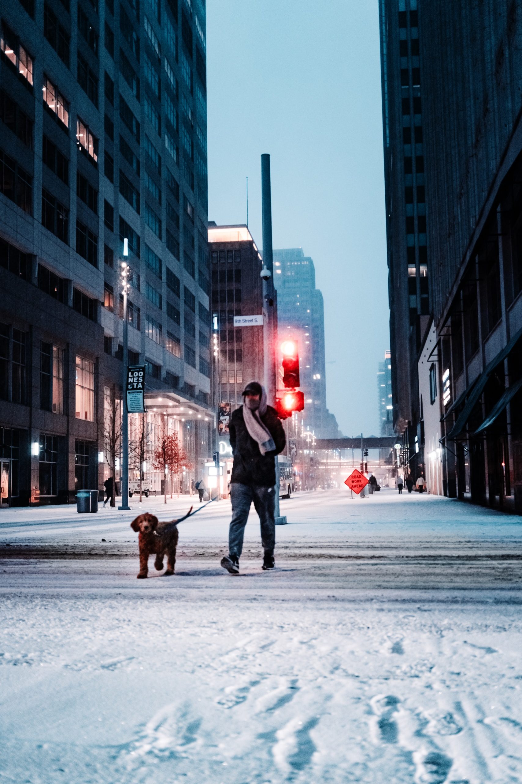 Man and his dog walking on a snow covered street in a city